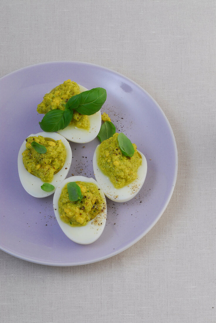 Four hard boiled eggs with pesto filling on lilac plate