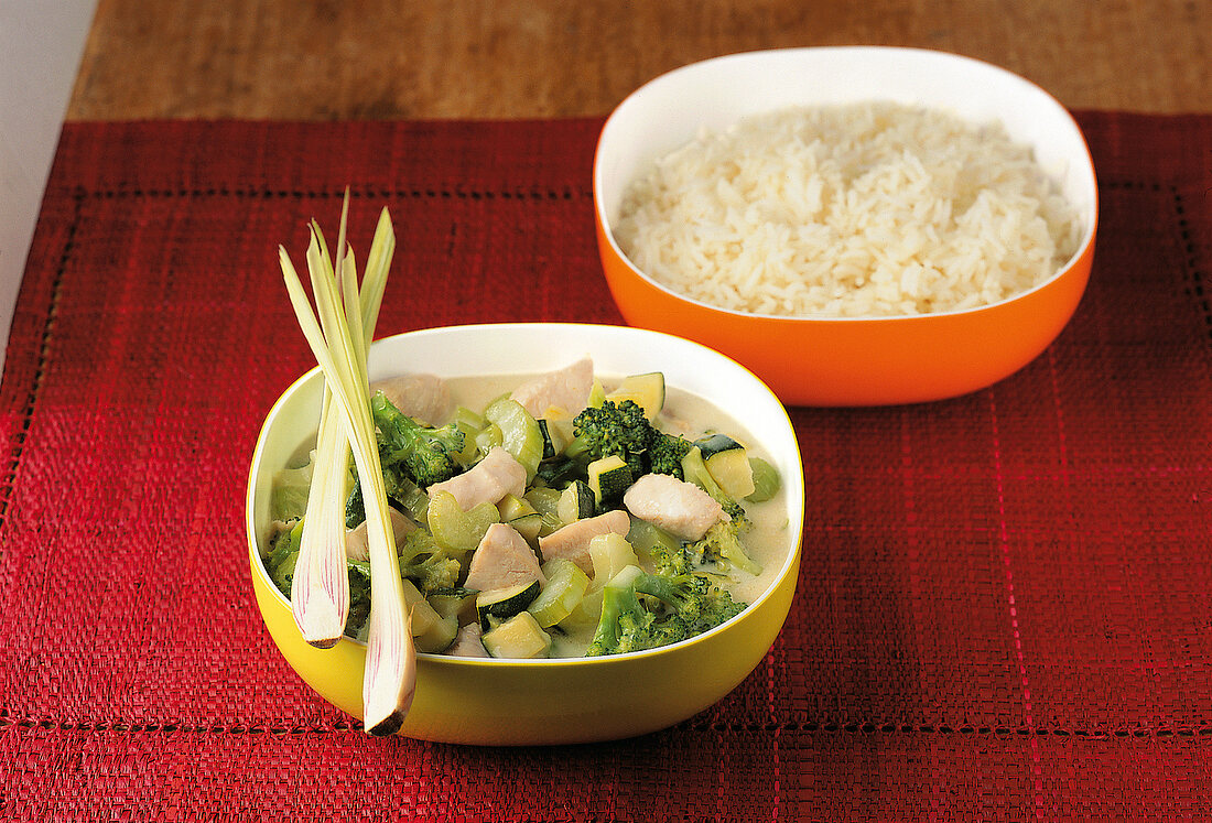 Thai chicken curry with broccoli in yellow bowl and basmati rice in orange bowl