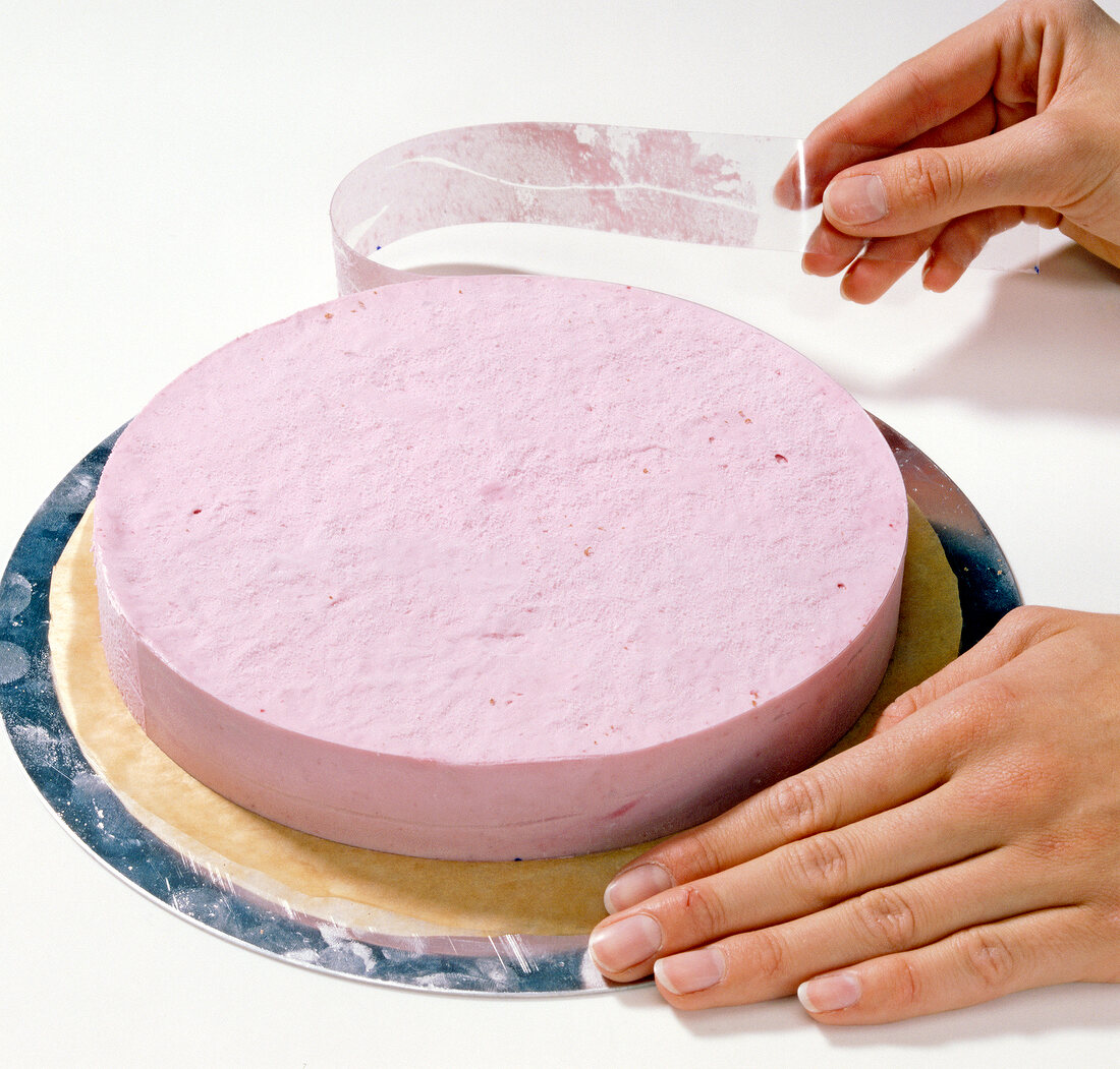 Close-up of hand pulling plastic strip from cake, step 3