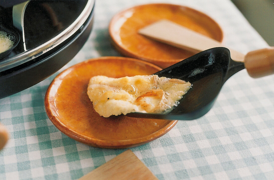 Raclette, Geschmolzener Käse vom Pfännchen auf kleinen Teller