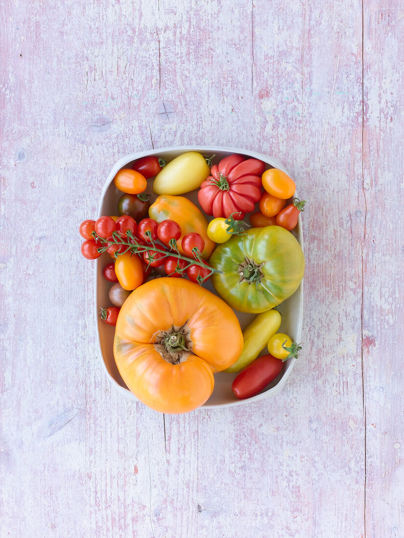 Different kinds of tomatoes in bowls and dishes on wooden table, overhead view