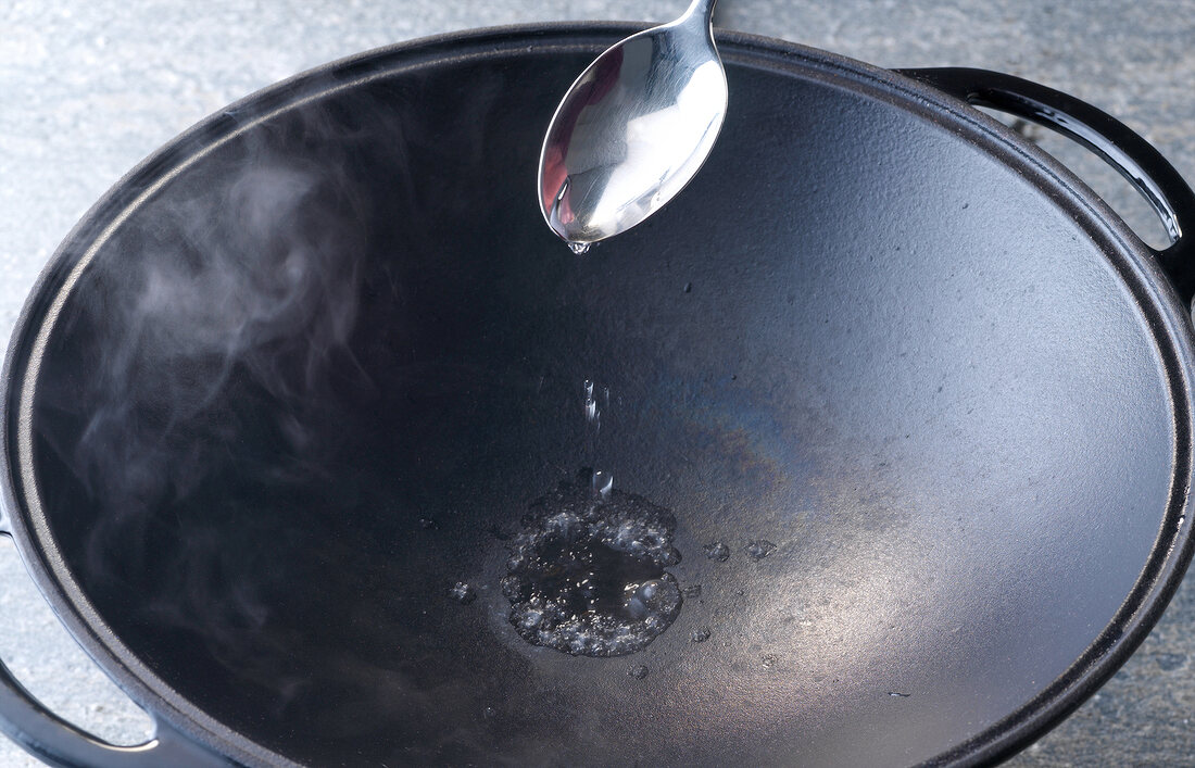 Checking temperature in wok by pouring water with teaspoon