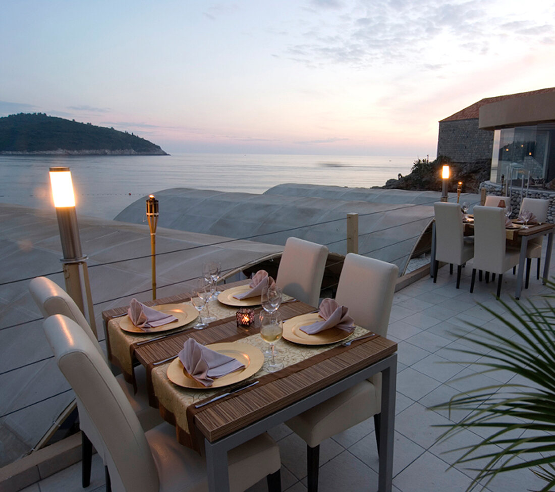 Tables laid on terrace besides illuminated torch at dusk