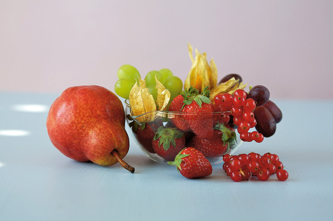 Strawberries, grapes, physalis and currants in bowl with pear on side