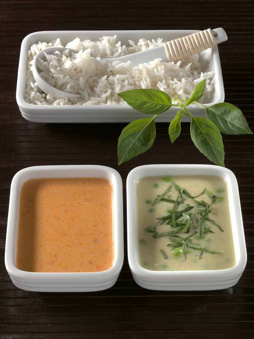 Green curry and peanut curry sauces with rice on wooden board