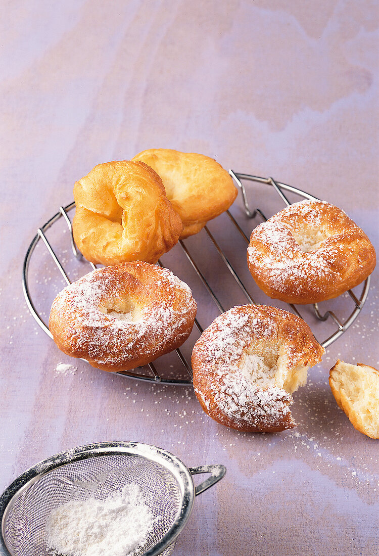 Backen, 5 frittierte Hefeküchlein auf Kuchengitter, Puderzucker