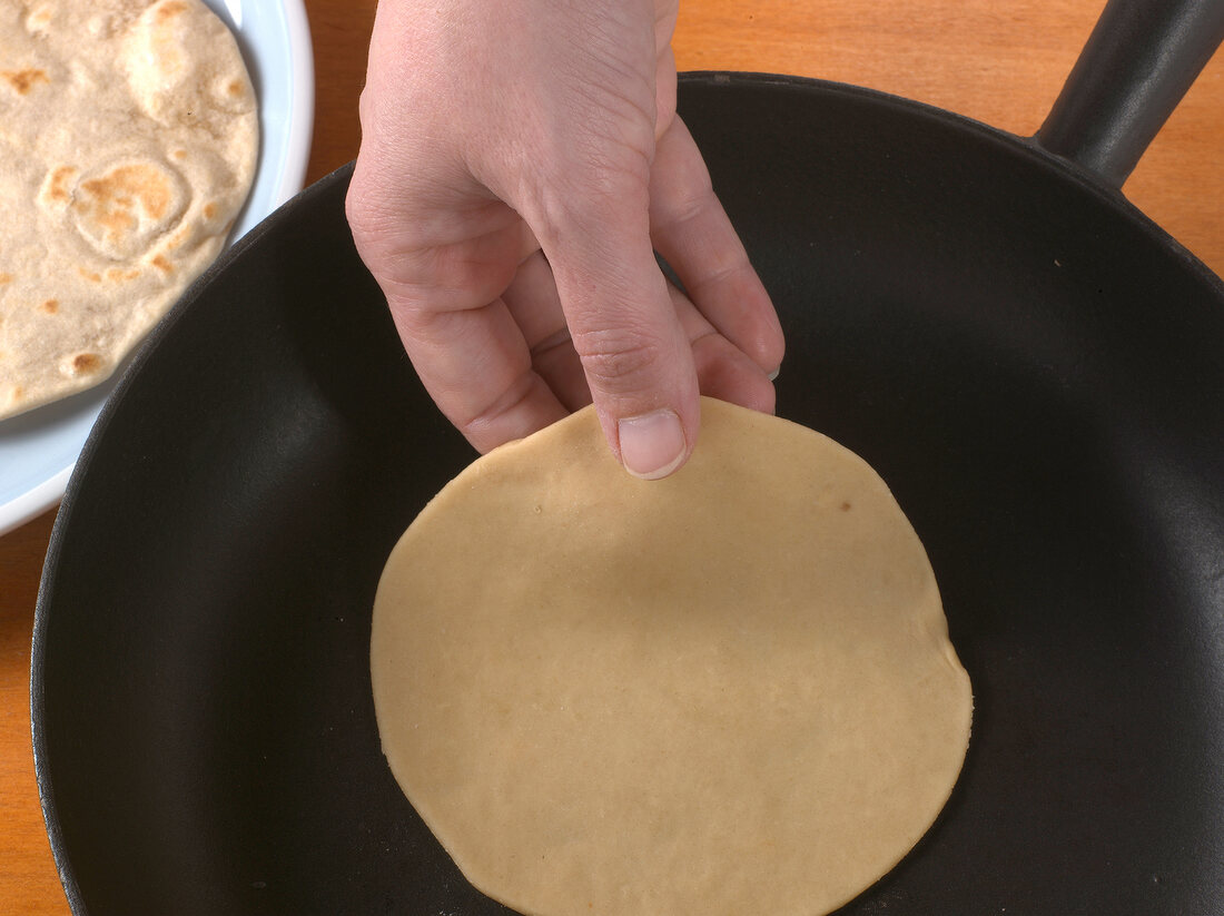 Dough in shape of circle being placed on pan for preparation of chapatti, step 2