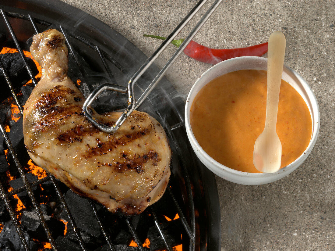 Chicken legs on grill with tongs and bowl of marinade