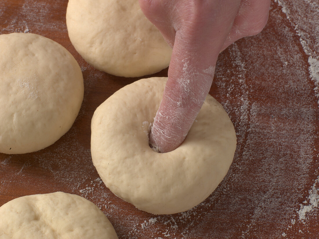 Hole being made in dough balls with finger for preparation of sesame bagel, step 2