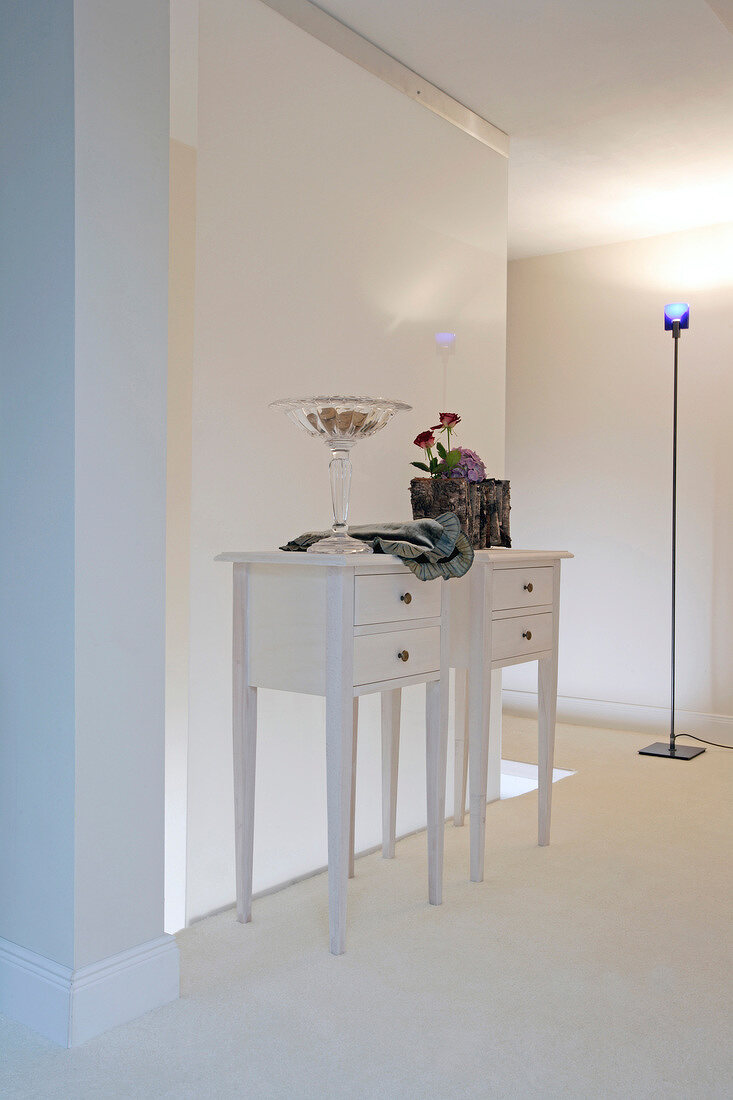 Two white dressers with drawers and floor lamp in a room with white painted wall