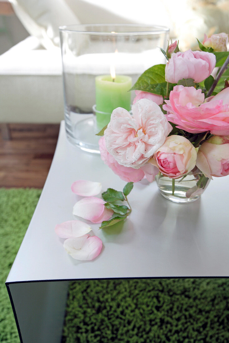 Close-up of bunch of pink roses in glass and green lit candle