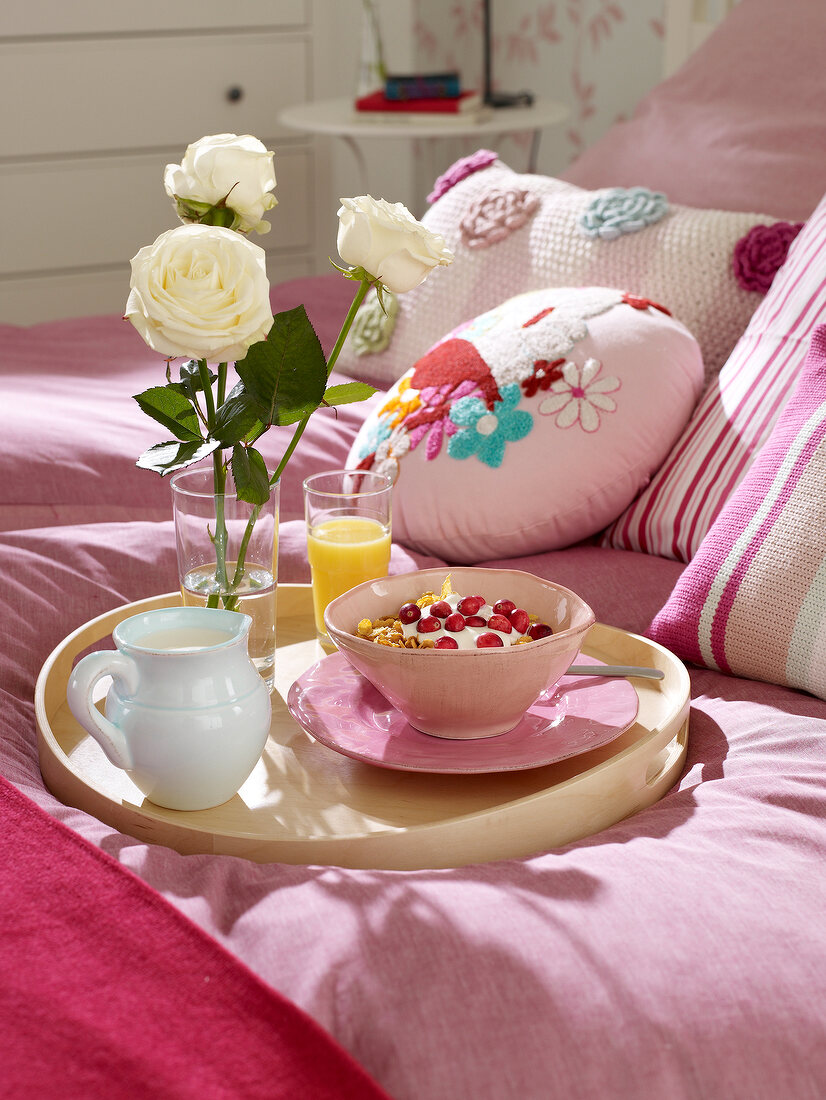 Breakfast tray with muesli, orange juice and roses on pink bed