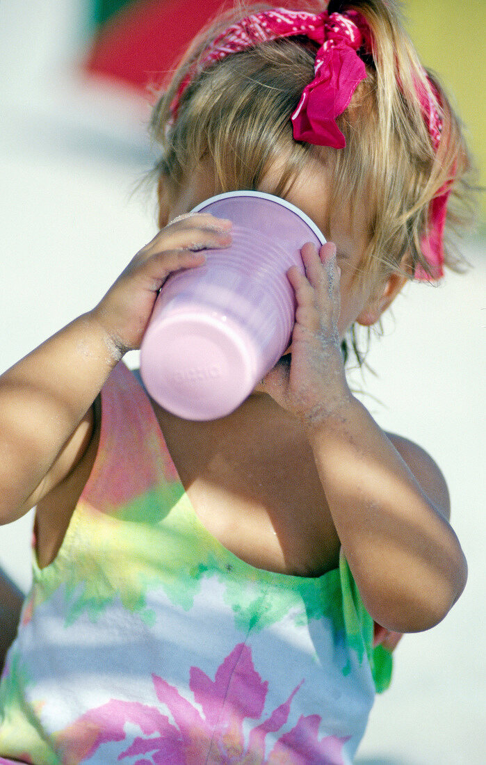 Portrait of cute girl wearing dress and red hairband holding a drink, smiling