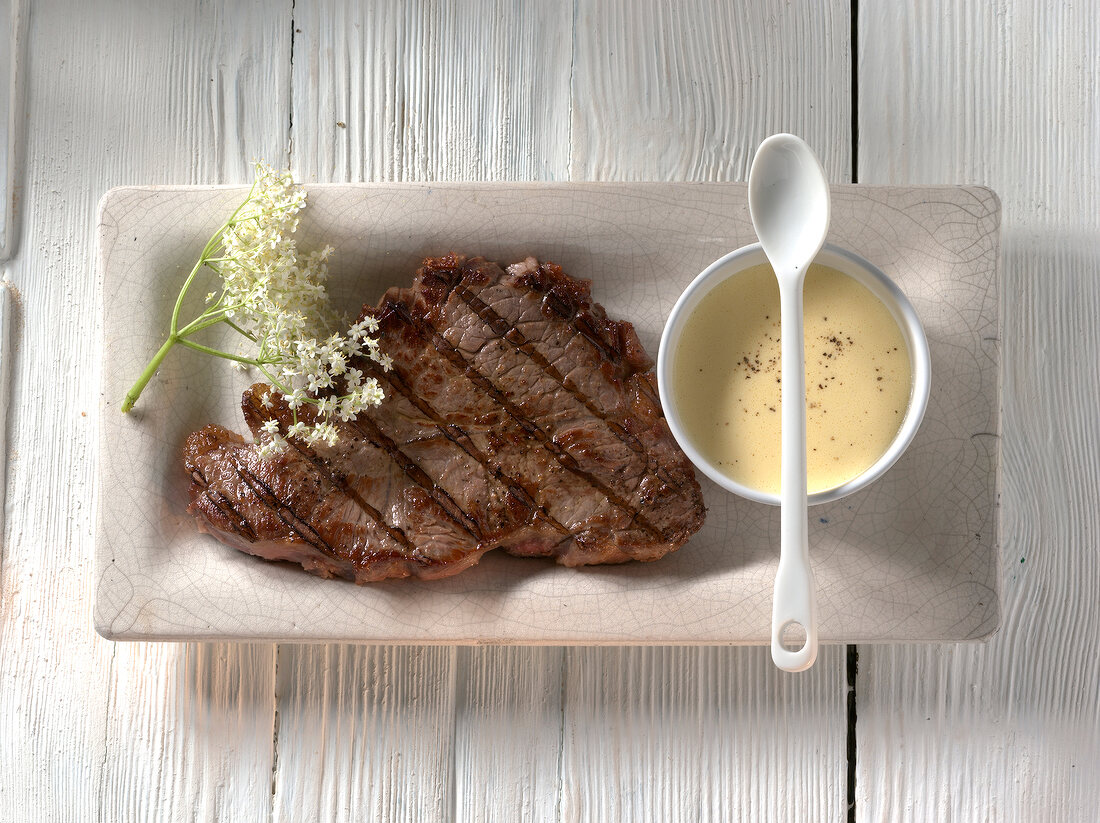 Bowl of hollandaise dip with beef steak and elderflower in serving dish