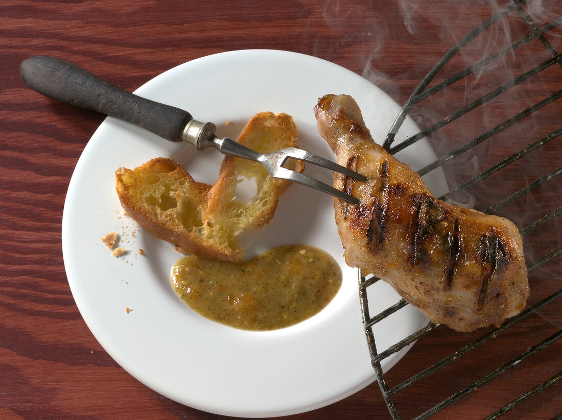 Grilled chicken leg on grill and bread and pineapple sauce on plate
