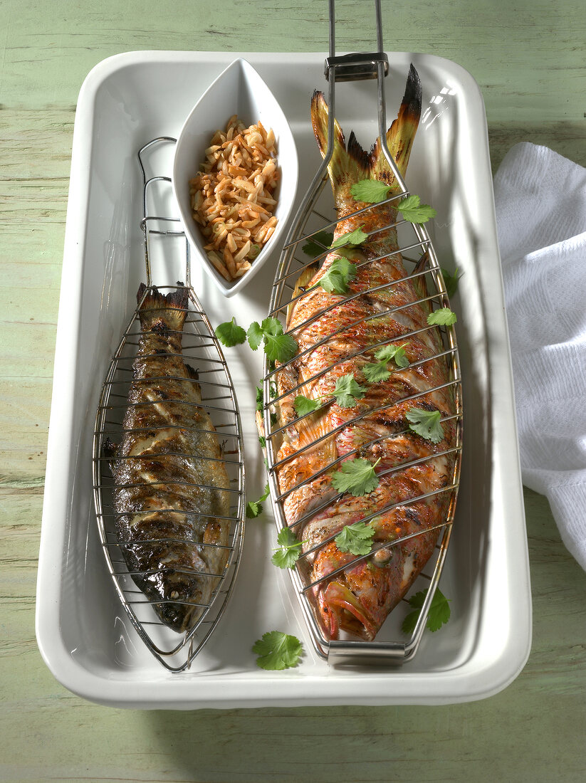 Trout and red snapper in fish grill with chopped almonds in bowl