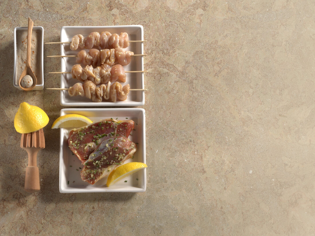 Four chicken skewers and two marinated lamb steaks with slices of lemon on plates