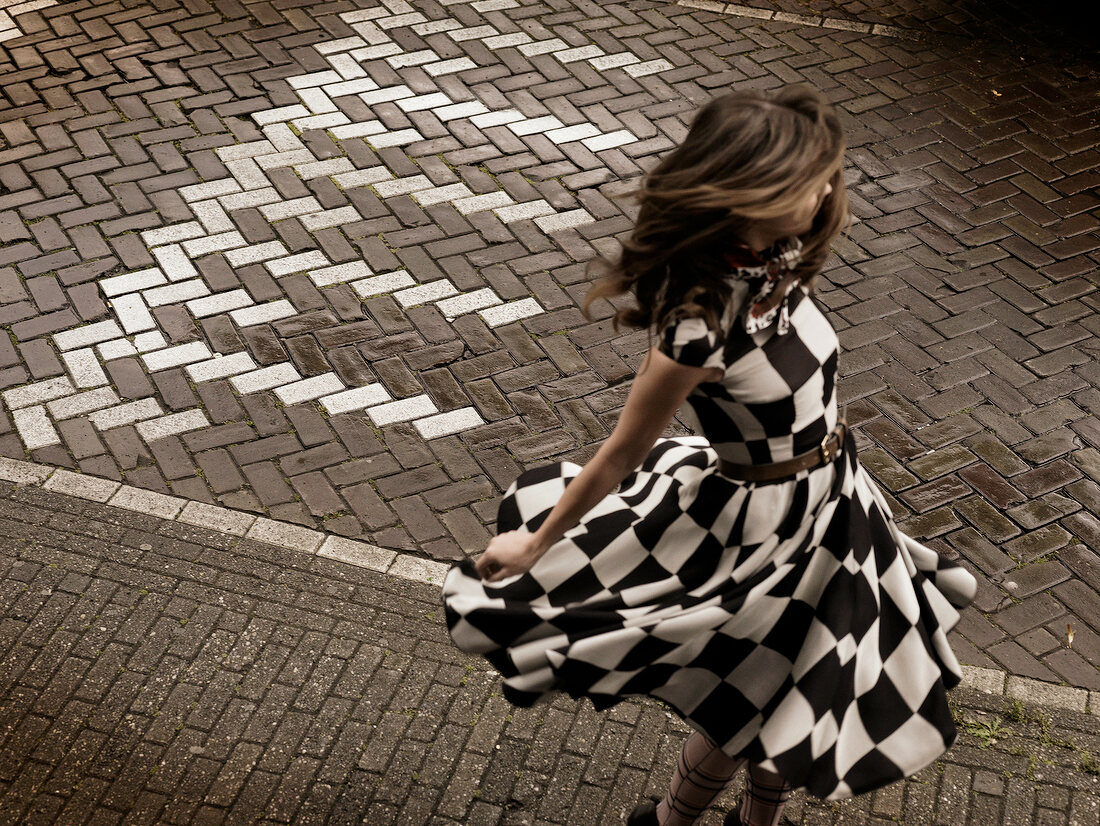 Woman with windswept hair wearing black and white pattern dress swirling on the street