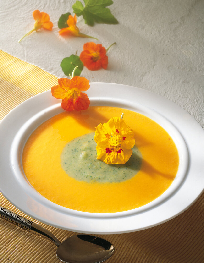 Carrot soup with zucchini mirror and nasturtium flowers in bowl