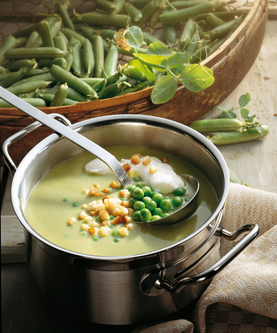 Pea soup with cream and croutons in pot with soup ladle