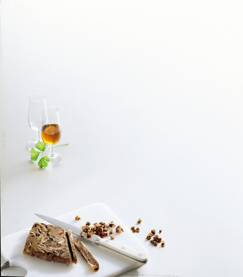 Pieces of beef on cutting board with glass of sherry on white background, copy space