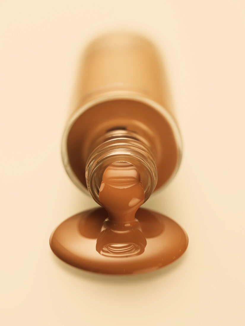 Brown make-up pouring out of bottle on white background