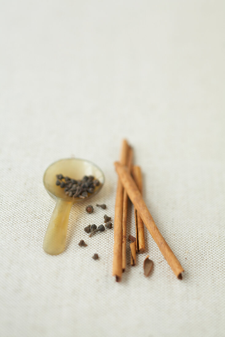 Three cinnamon sticks and spoon of cloves on white background
