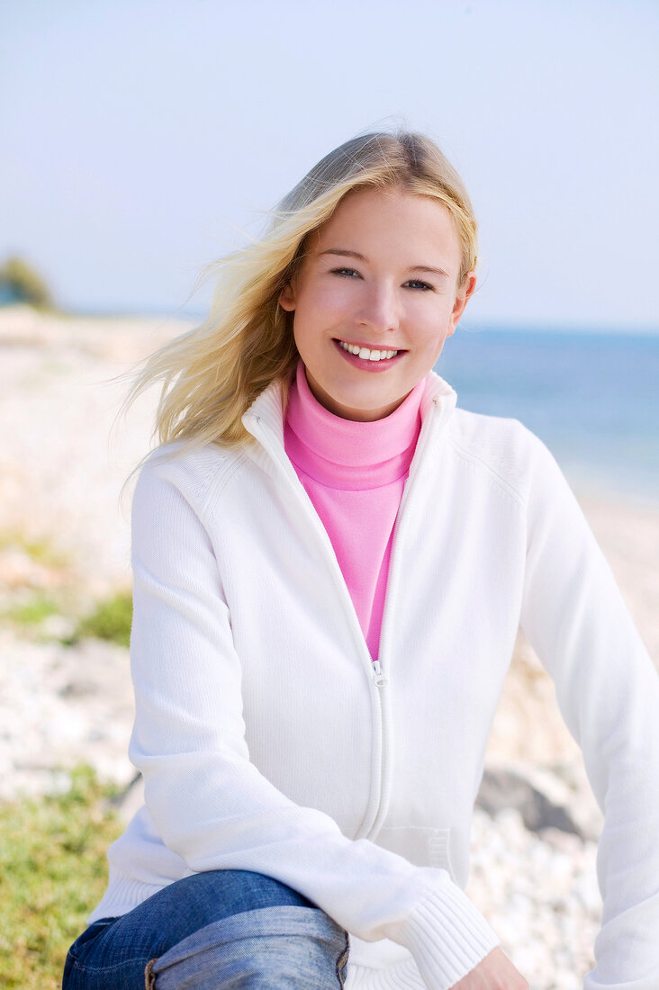 Portrait of beautiful blonde woman in white jacket over pink turtleneck t-shirt, smiling