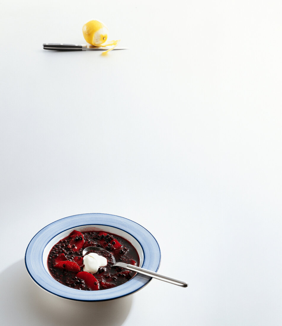 Cold elderberry soup with apples and creme fraiche on plate on white background