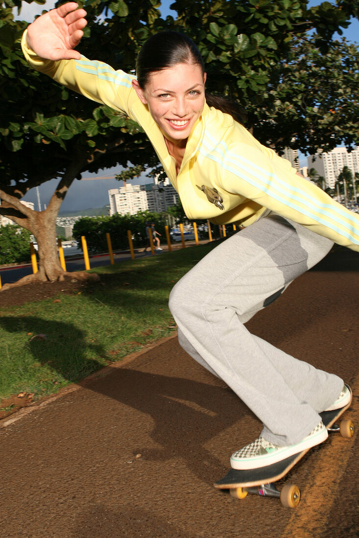 Black-haired woman in a yellow sweater on a skateboard