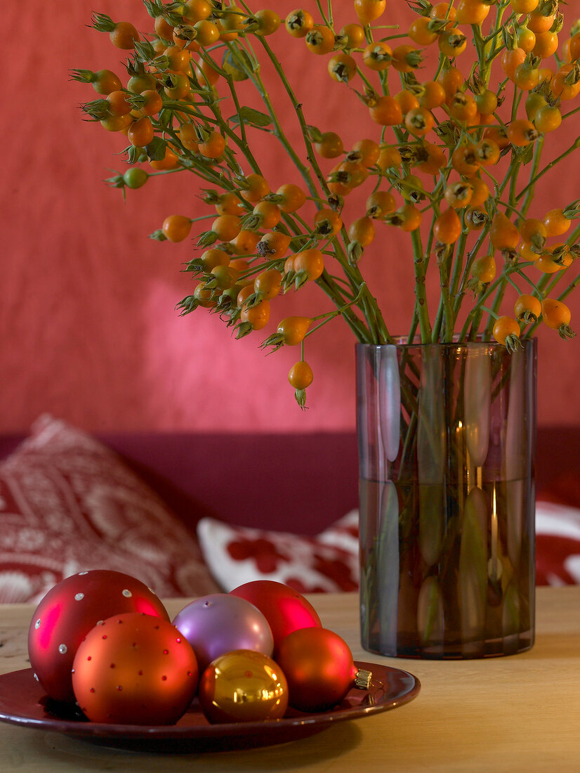 Rose hip branches in vase and baubles in bowl in front