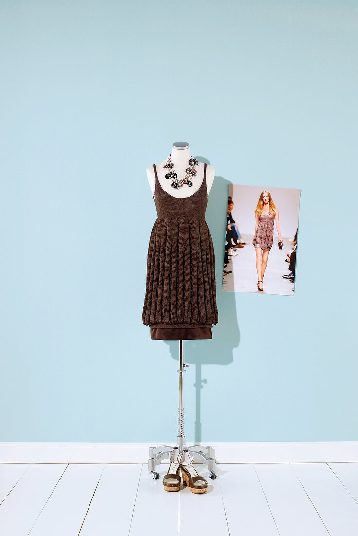 Brown knit dress with necklace hanging on mannequin against blue background