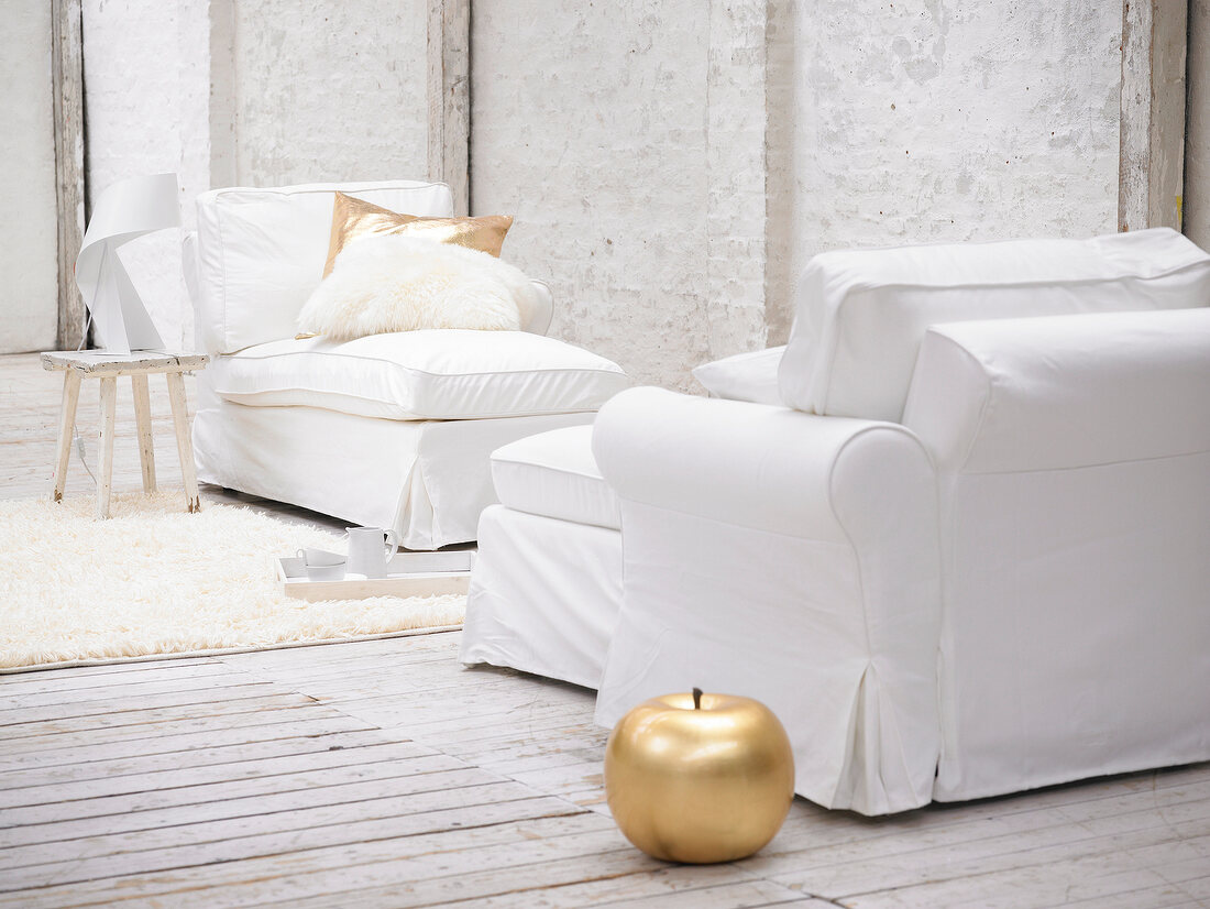 White sofa and armchairs with pillows and gold ceramic apple on carpet