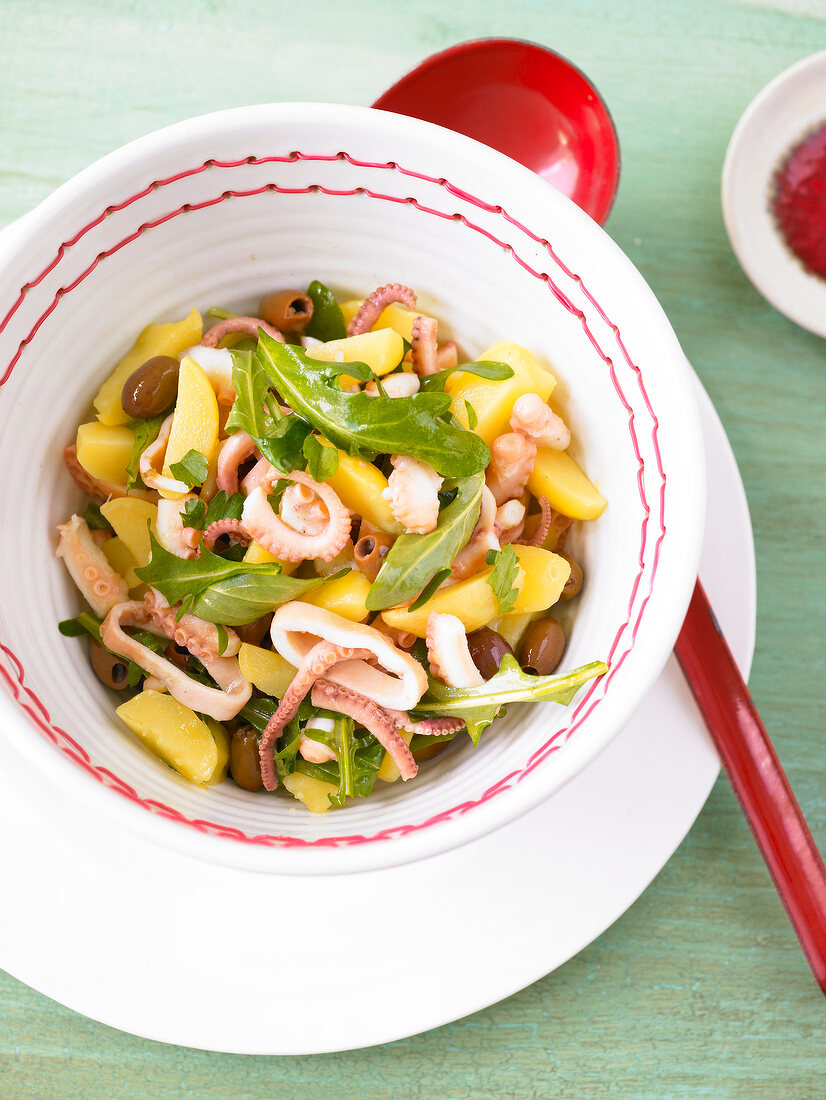 Octopus salad with potatoes, olives and rocket in bowl