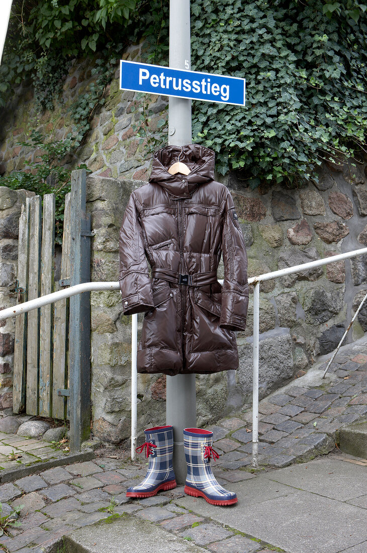 Brown down coat hanging on street pole and rubber boots on side