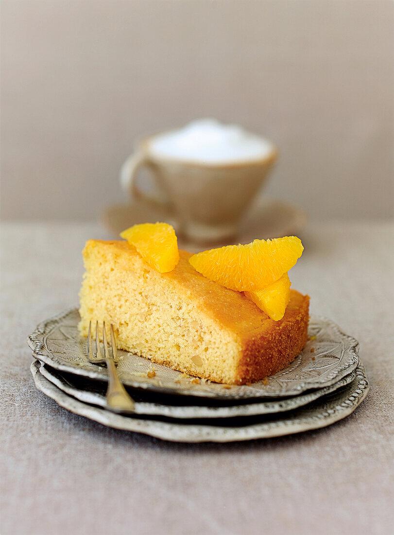 Piece of orange cake with saffron syrup and orange segments on plate with cake fork