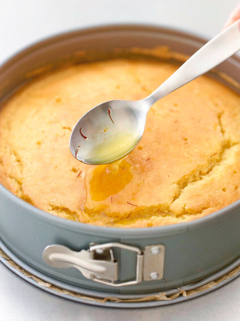 Close-up of saffron syrup being poured on orange cake with spoon