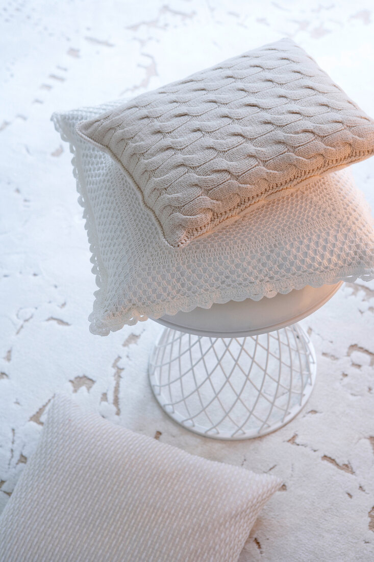 Three white pillows knitted with cable knit and crochet lace