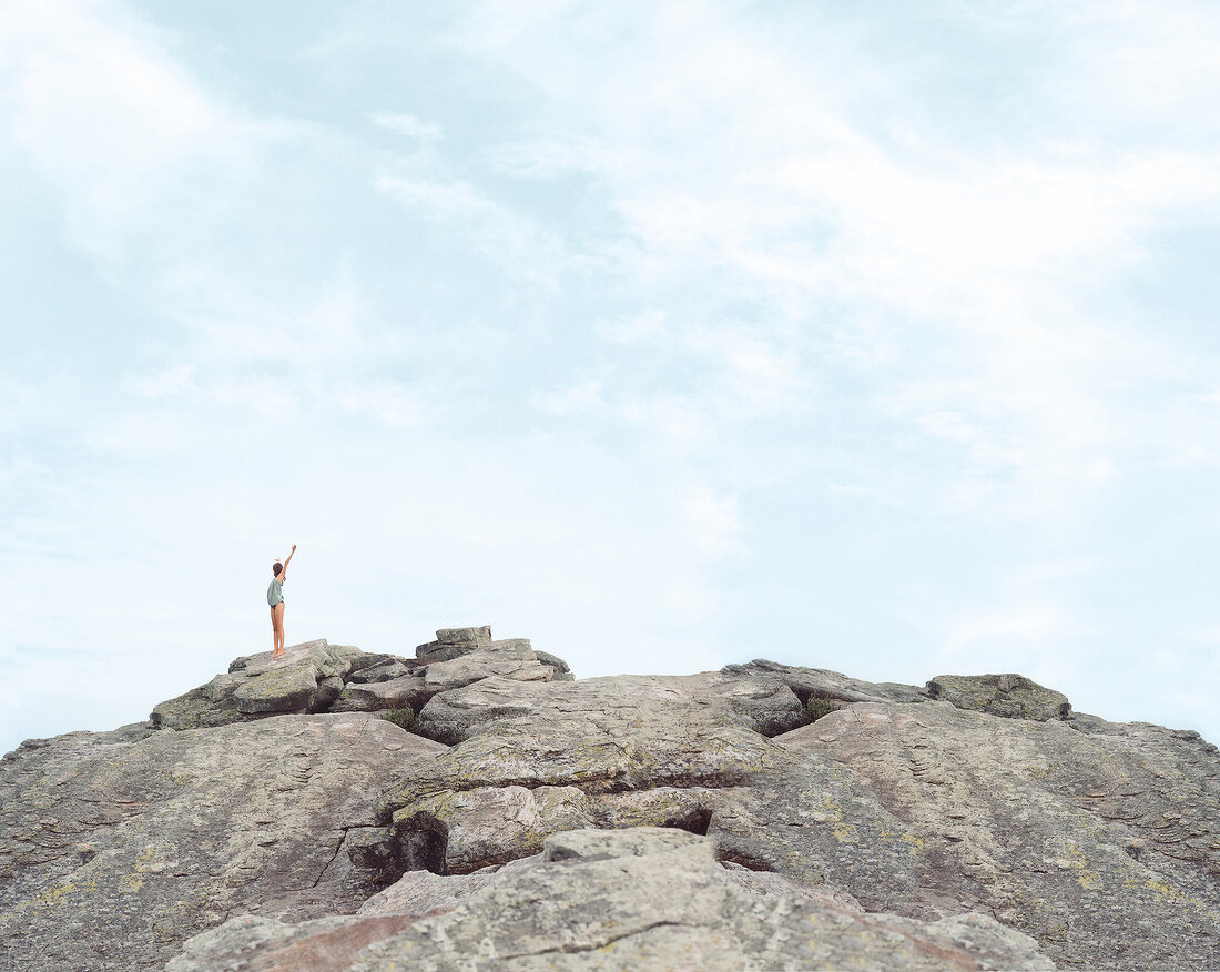 Frau im Bikini und Shirt, steht auf Felsen, Arme nach oben
