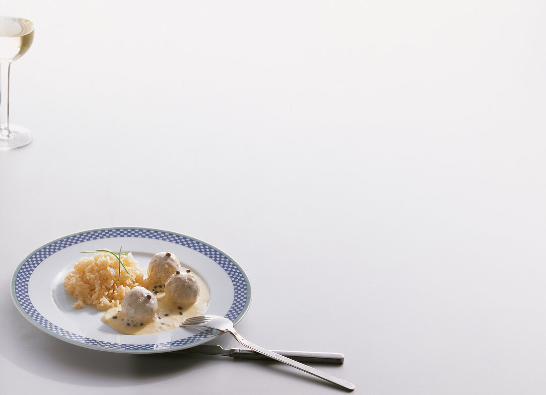 Meatballs in white wine cream sauce with rice and capers on white background