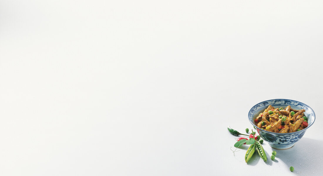 Beef with peas peppers and coconut milk curry in bowl on white background