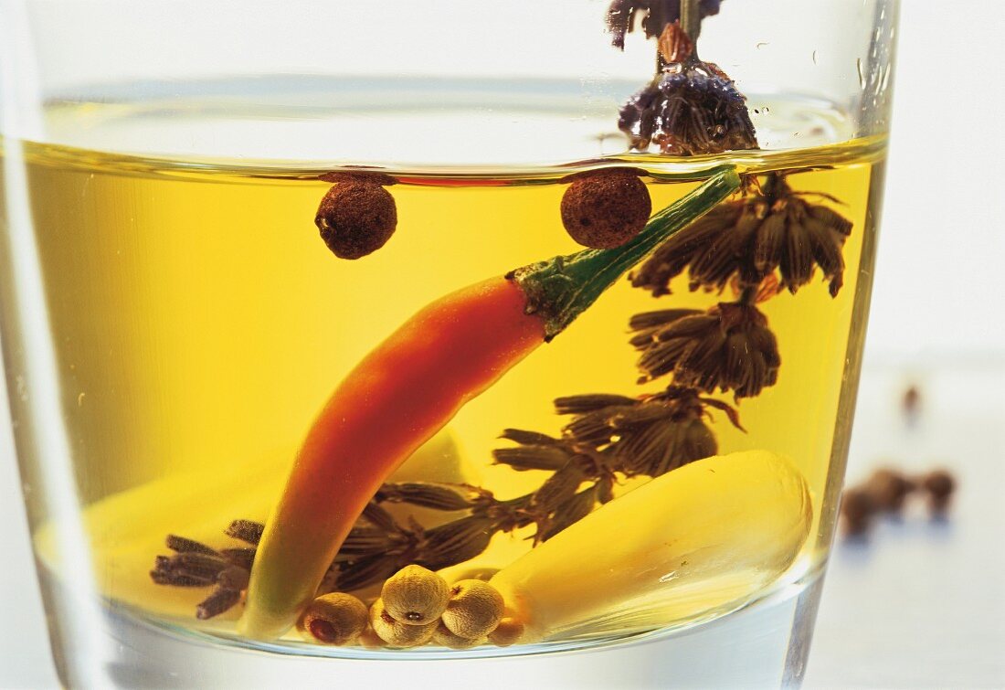 Spices, a chilli pepper and a sprig of lavender preserved in oil (close-up)