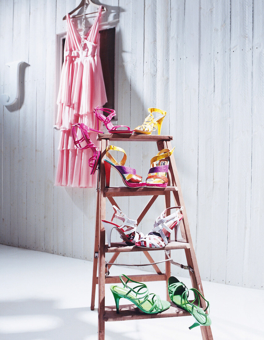Various shoes arranged on ladder with pink dress on hanger in background