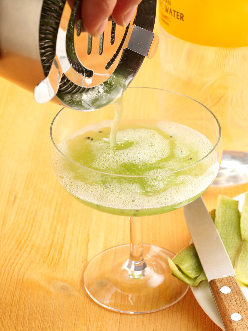 Kiwi cocktail being poured into cocktail glass