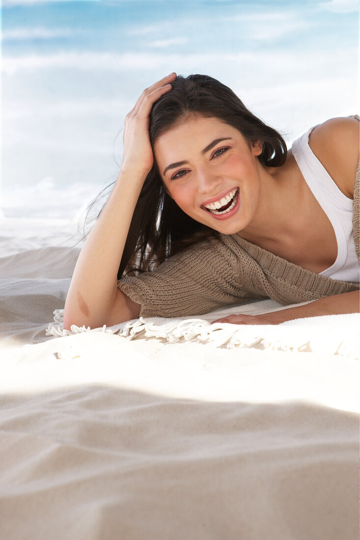 Frau liegt im Sand auf einer Deck und stützt ihren Kopf auf
