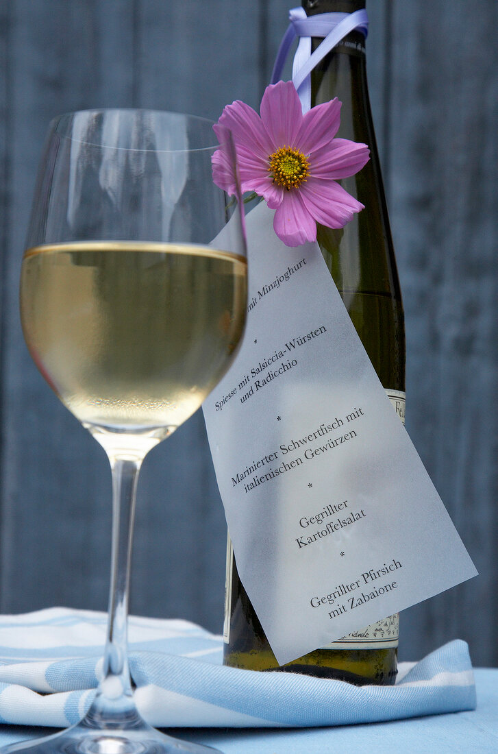 Close-up of wine glass, bottle and menu with flower