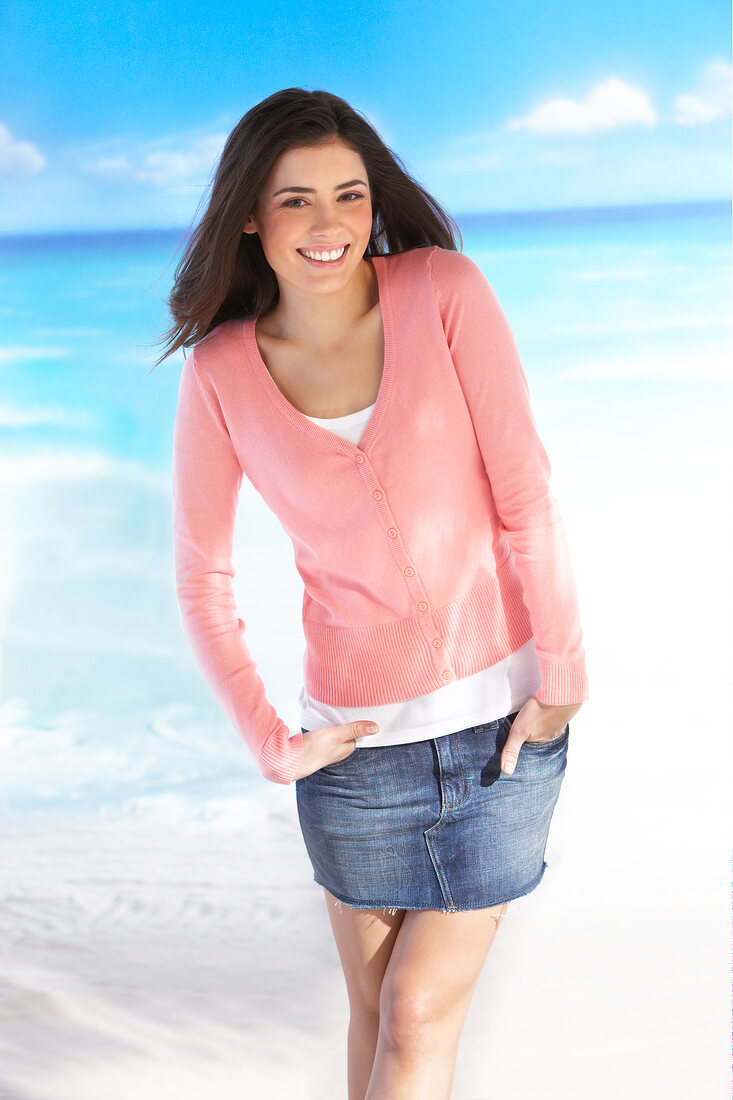 Portrait of happy woman wearing pink cardigan and denim skirt on the beach, smiling