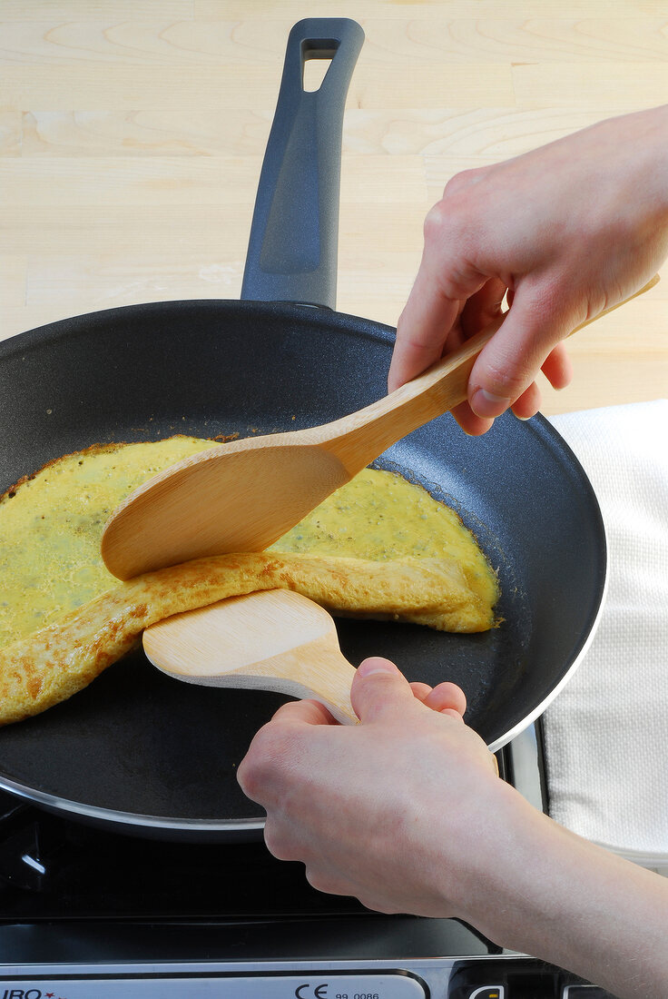 Omelette being rolled up with two flat wooden spoons in frying pan, step 3