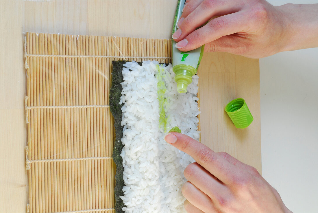 Spinach sauce being put on rice for preparation of sushi on sushi mat, step 2