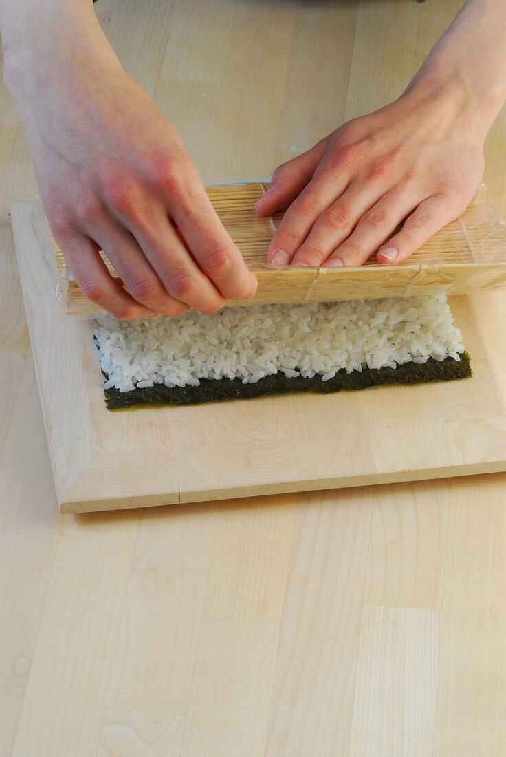 Placing sushi mat on bed of rice for preparation of sushi, step 2